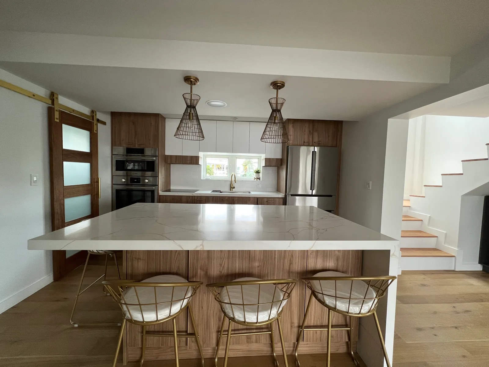 Open kitchen — walnut cabinetry, marble waterfall island, gold pendants